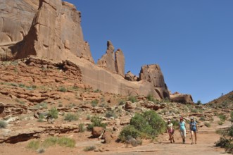 Several people are hiking in a dry, rocky landscape called Wall Street, under a bright blue sky,