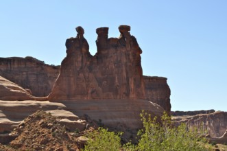 Three Gossips, a majestic red sandstone rock formation rising above a bright blue sky, Arches