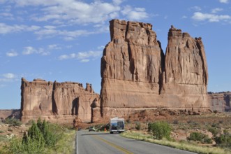 A road leads through a desert landscape with impressive sandstone formations and isolated vehicles