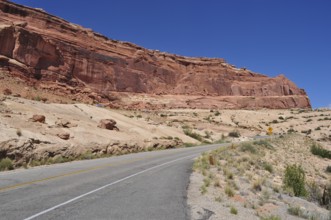 Road leading past a barren, red rock formation under bright blue sky, Arches National Park, Utah,