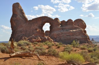 Turret Arch, a natural rock arch rising against a blue sky with scattered clouds in the red desert,