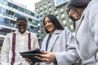 Diverse business colleagues smiling and laughing while collaborating over a tablet outdoors by