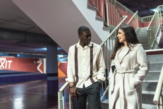 Young diverse couple walking up a concrete staircase in an underground parking facility, engaged in