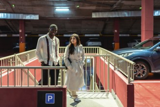 Diverse interracial couple walking up concrete stairs in an urban parking garage, smiling and