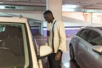 Young black man in an underground parking garage smiling as he opens his white car door, confident