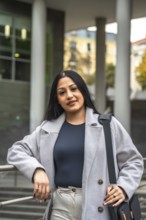 Confident indian woman showing her elegant business casual style, leaning on a railing in an urban