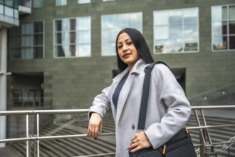 Professional latin woman standing by a railing with a messenger bag, looking at the camera against