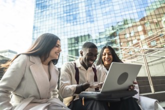 Group of diverse coworkers laughing while sharing content and collaborating on a laptop during an