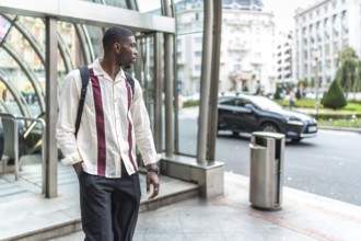 Young black man carrying a backpack and wearing a stylish shirt, standing confidently on a city