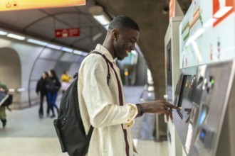 Young man standing at an automated ticket machine, smiling, and touching the screen while