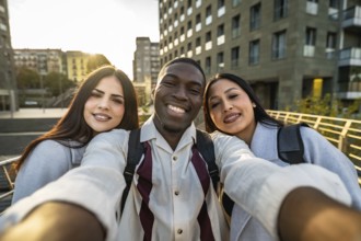Three diverse students smiling into a smartphone, taking a city street selfie while walking and