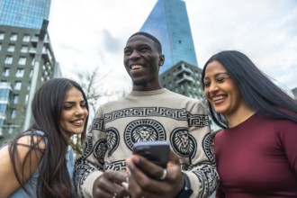 Diverse group of young adult friends laughing, smiling, and happily sharing content on a smartphone