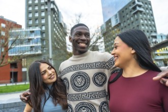 Diverse group of three young friends walking together on a city street, one man embracing two