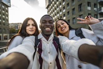 Three smiling multiracial friends enjoying an outdoor moment, capturing a joyful selfie together in