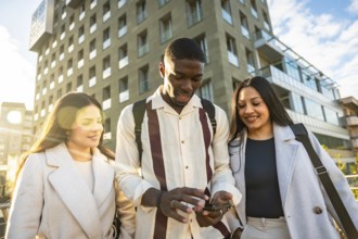 Young diverse friends walking in the city, smiling and gathered around a smartphone, sharing