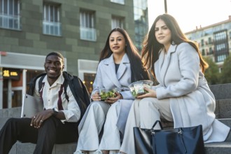 Diverse colleagues sitting on steps and smiling while enjoying healthy salads during a casual urban