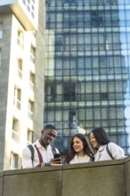Three diverse students, a man and two women, smiling and looking at a smartphone, sharing content