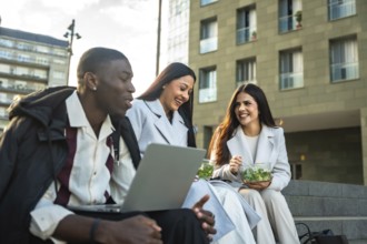 Three smiling diverse business people sitting on city stairs, discussing work and happy together