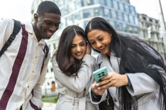 Diverse group of young adult friends smiling and laughing while watching something on a smartphone