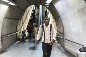 Young man with backpack walking confidently through a modern subway tunnel past escalators and