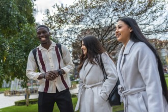 Multiracial young adults walking together in an urban park, smiling and happily conversing, showing