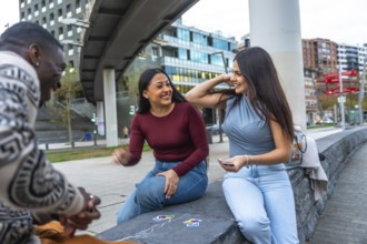 Happy diverse friends sitting in an urban park, playing cards and laughing together, enjoying