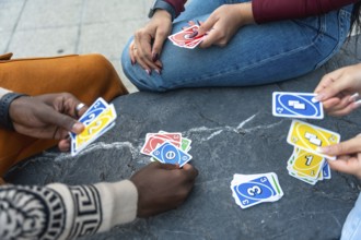 Diverse people gathering outdoors, playing a popular card game, throwing cards onto the stone