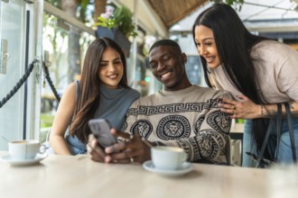 Multi ethnic friends enjoying coffee, sharing a cheerful moment while looking at a smartphone