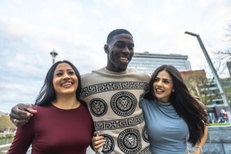 Diverse group of three happy young friends, a black man embracing two hispanic women, walking