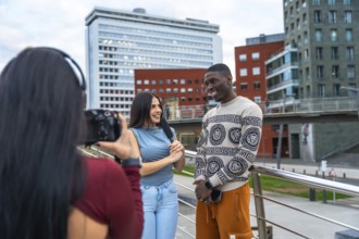 Journalist holding a microphone and talking with a smiling young man while a videographer is