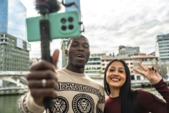 Diverse interracial couple vlogging with a smartphone on a selfie stick, smiling as they record