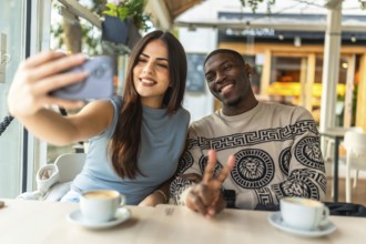 Smiling diverse couple making a peace sign gesture while taking a selfie with a smartphone at a