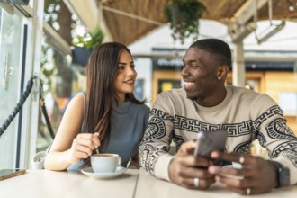 Diverse couple smiling and interacting joyfully, sharing a relaxed moment together at a cafe while