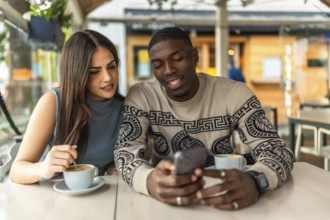 Young diverse couple enjoying a moment together at a cafe, discussing content on a smartphone and