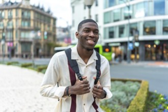 Young black man with a backpack smiling at the camera on a city street, exploring urban