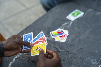 Hands holding a colorful fan of playing cards over a stone table during a casual indoor card game,