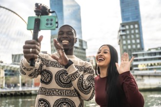 Happy young multiracial couple creating content with a smartphone on a selfie stick, streaming live