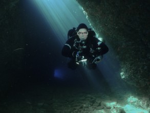 A diver with equipment floats through the interior of a blue-lit cave. Fraskeric dive site, Stoja,