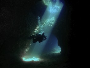 A diver floats through a mystical underwater cave, flooded with blue light. Fraskeric dive site,