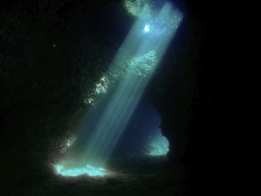 Sun rays illuminate the interior of a dark underwater cave with blue light reflections. Fraskeric