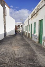 Narrow cobblestone street in Arrecife, Lanzarote, in portrait mode. On the left the back of the