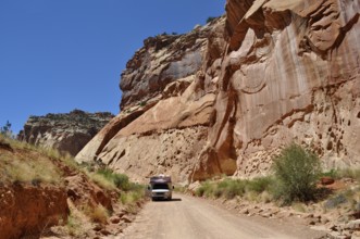 A camper drives along a dirt road in a canyon with red rock walls, Capitol Reef National Park,