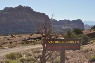 Desert landscape with vehicle length road sign and rocky mountain range in the background, Capitol