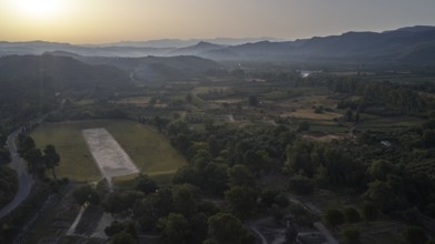 Ancient stadium in the morning backlight, wide landscape at sunset with hills and a large