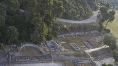 Old theatre and ruins next to a road surrounded by dense nature, drone shot, archaeological site,