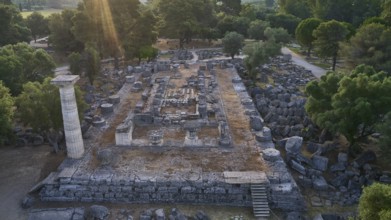 Temple of Zeus in backlight, ancient ruins surrounded by trees, with a stone column and