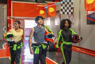 Diverse friends preparing for a go kart race, holding helmets and wearing race suits, walking