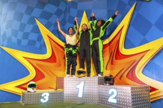 Three friends, dressed in race overalls, raising their arms and celebrating their achievement and