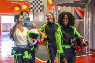 Diverse group of young adult friends wearing racing suits and holding helmets, posing for a