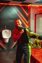 Smiling young man in neon lit restroom pulling on black and green karting jumpsuit, getting dressed